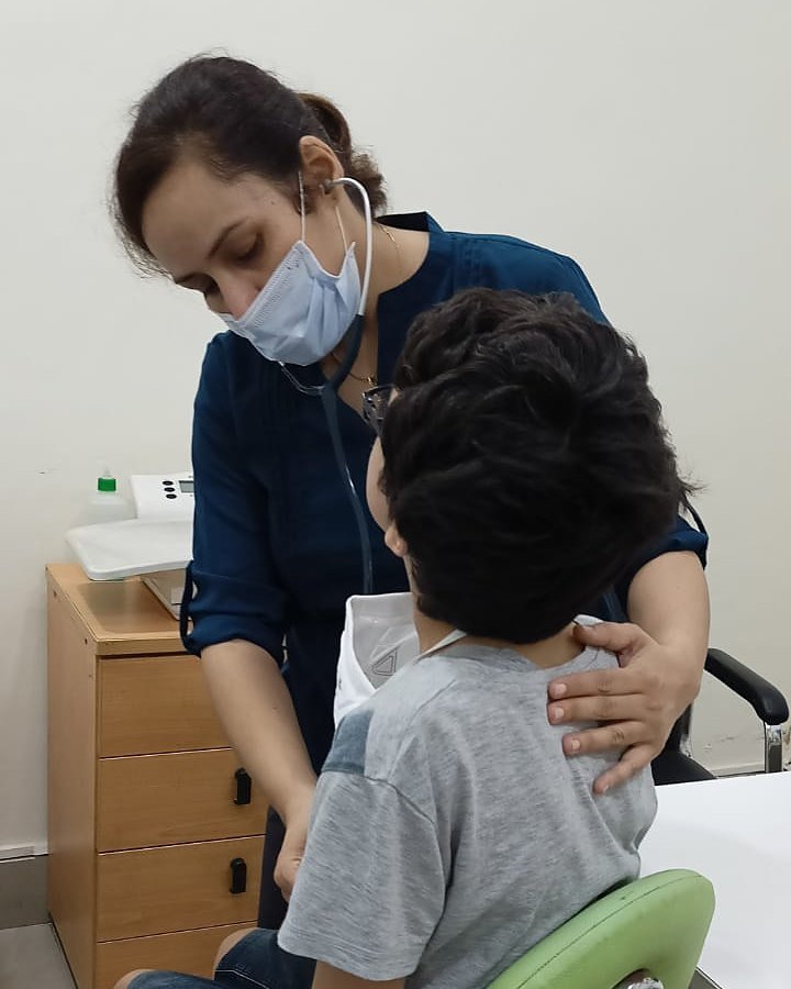Dr. Preeti Chadha listening to a young patient's chest with a stethoscope